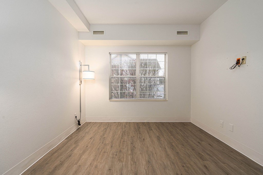 an empty room with white walls and wood flooring and a window